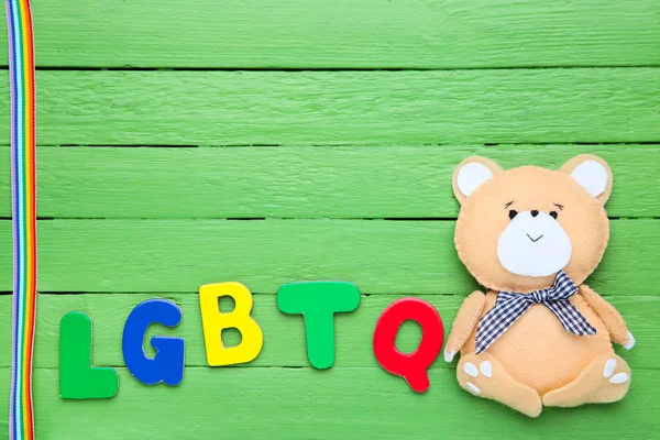 Abbreviation LGBT with soft bear toy on green wooden table