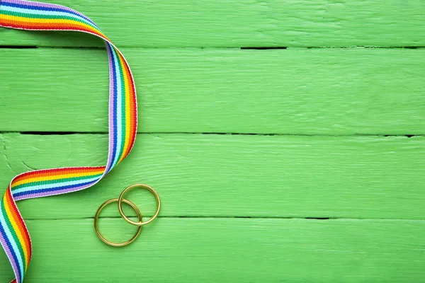 Rainbow ribbon with golden rings on green wooden table