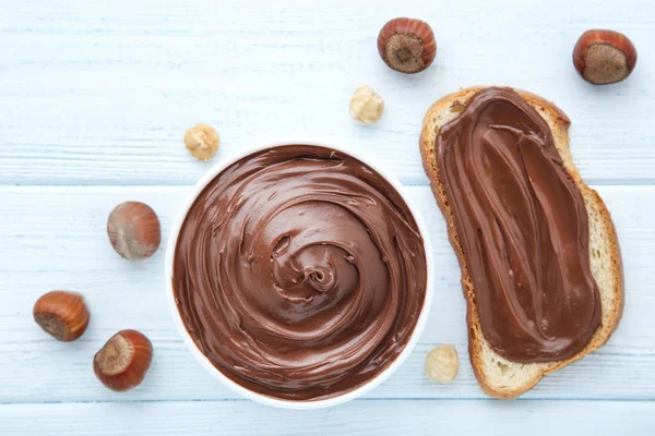 Roti dengan coklat cair dan hazelnut di atas meja kayu — Stok Foto