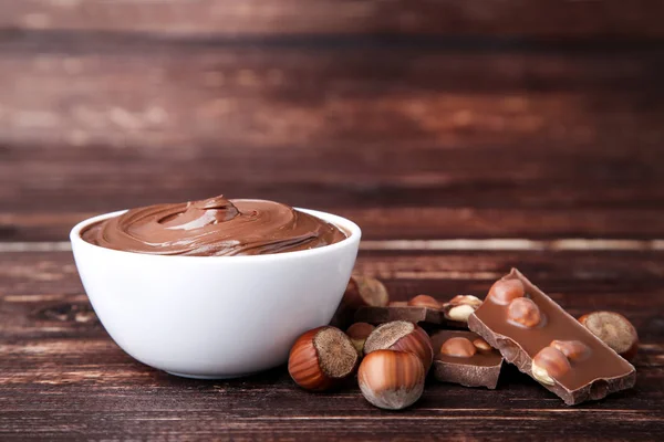 Melted chocolate with hazelnuts on brown wooden table — Stock Photo, Image