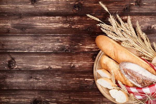 Baguettes frescos con espigas de trigo sobre mesa de madera marrón — Foto de Stock