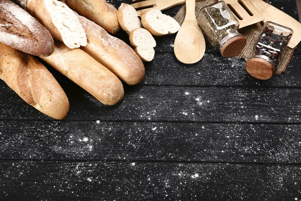 Frische Baguettes mit Gewürzen und Küchenbesteck auf schwarzem Woo — Stockfoto