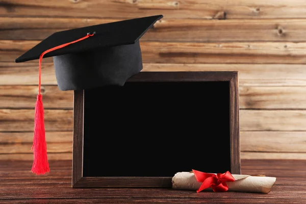 Czapka maturowa z dyplomem i pustą ramą na brązowym drewnianym TABL — Zdjęcie stockowe