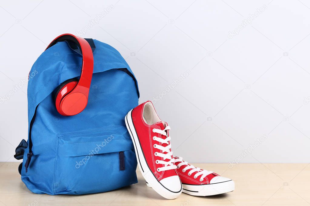 School backpack with headphones and sneakers on grey background