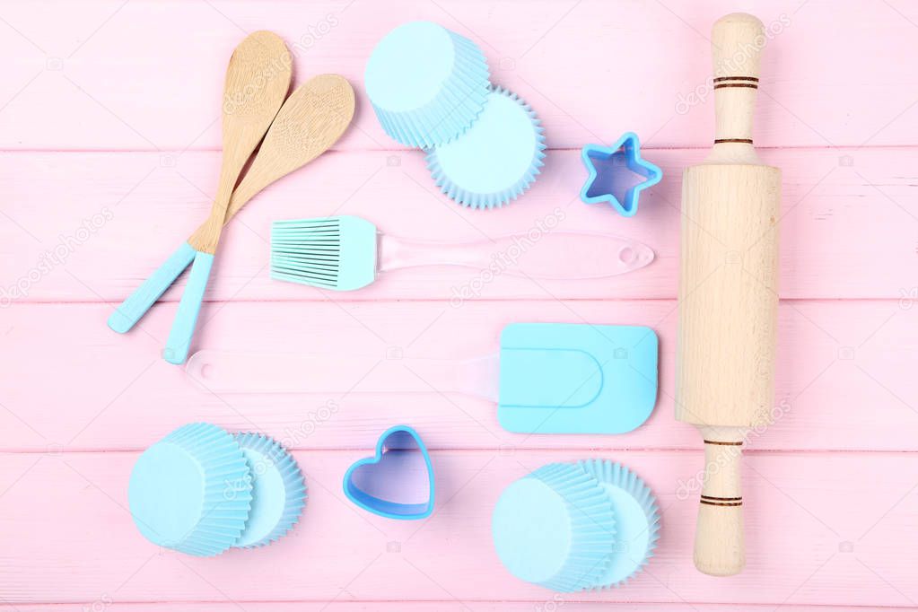 Cupcake cases with kitchen utensils on pink wooden table