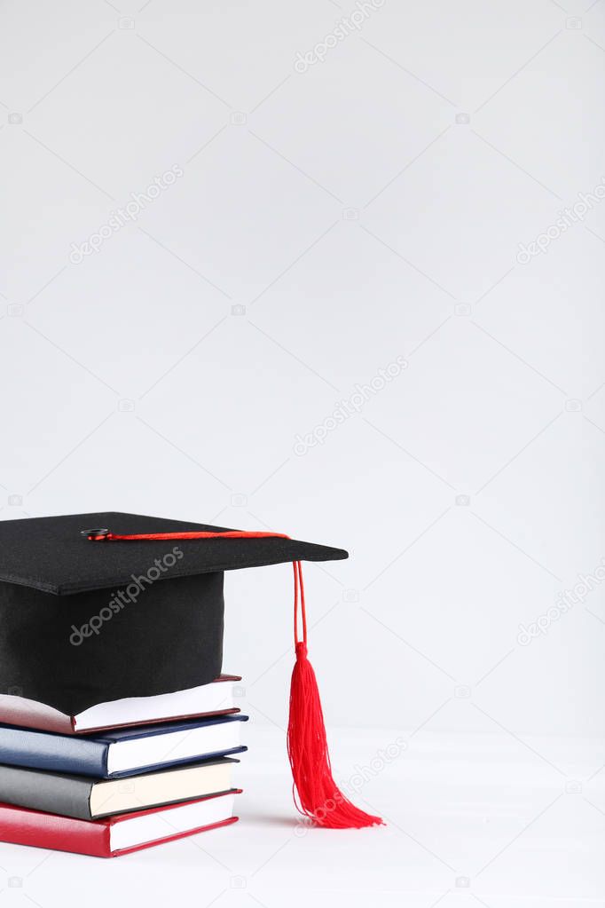 Graduation cap with stack of books on grey background