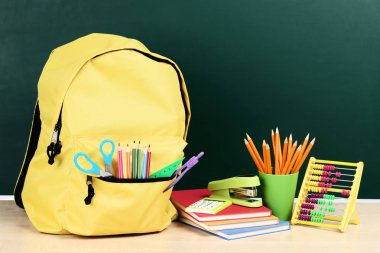 Yeşil arka planda okul malzemeleriyle dolu sırt çantası.