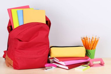 Gri arka planda okul malzemelerinin olduğu sırt çantası.