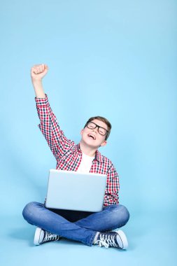 Mavi arka planda oturan bir dizüstü bilgisayar ile genç çocuk