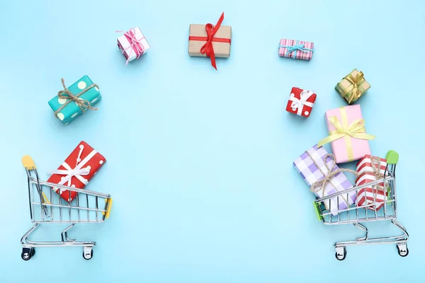 Mavi arka plan üzerinde hediye kutuları ile küçük alışveriş arabaları — Stok fotoğraf