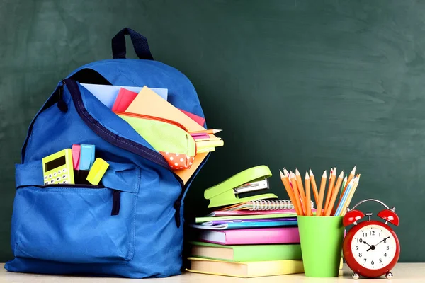 Mochila con útiles escolares sobre fondo verde —  Fotos de Stock