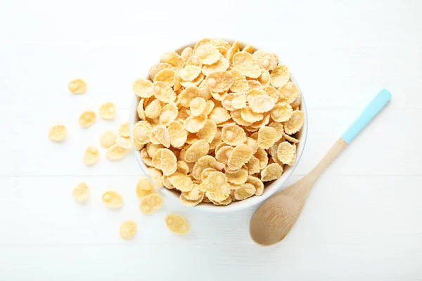 Copos de maíz en tazón con cuchara sobre mesa de madera blanca — Foto de Stock