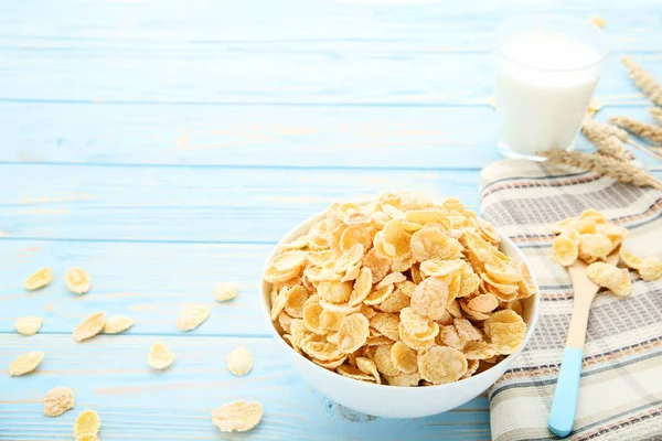 Corn flakes in bowl with spoon and glass of milk on wooden table