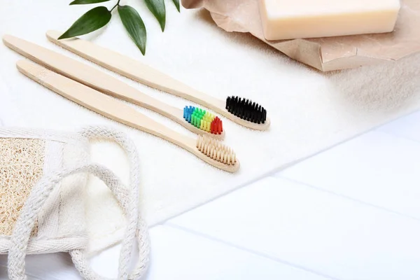 Bamboo toothbrushes with towel, washcloth and green leafs on white wooden table — Stock Photo, Image