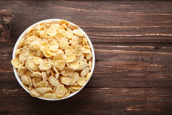 Corn flakes in bowl on brown wooden table — Stock Photo, Image