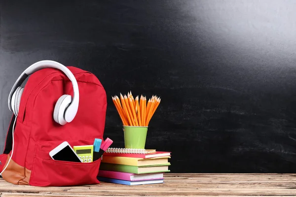 Mochila con útiles escolares y auriculares sobre fondo negro — Foto de Stock