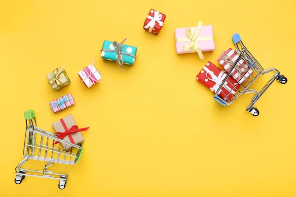 Sarı arka planda hediye kutuları olan küçük alışveriş arabaları — Stok fotoğraf