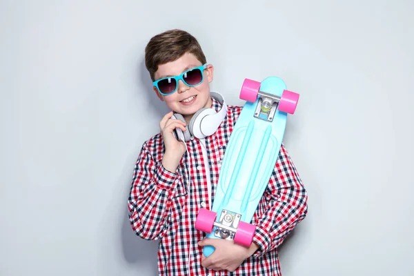 Niño con auriculares sosteniendo monopatín sobre fondo gris — Foto de Stock