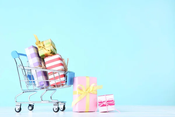 Pequeño carrito de compras con cajas de regalo sobre fondo azul — Foto de Stock