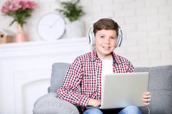 Молодий хлопчик з ноутбуком і навушниками сидить на дивані — стокове фото