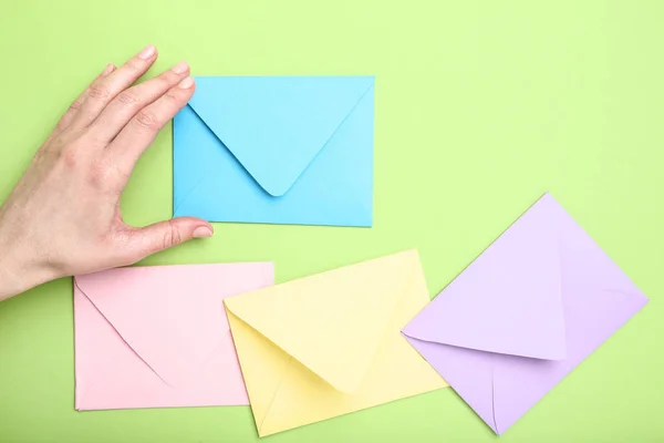 Female hand with colorful paper envelopes on green background — Stock Photo, Image