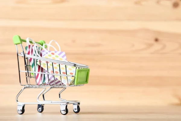 Small metal cart with shopping bags on brown wooden table — Stock Photo, Image