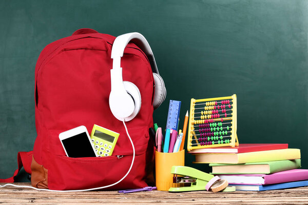 Backpack with school supplies on green background