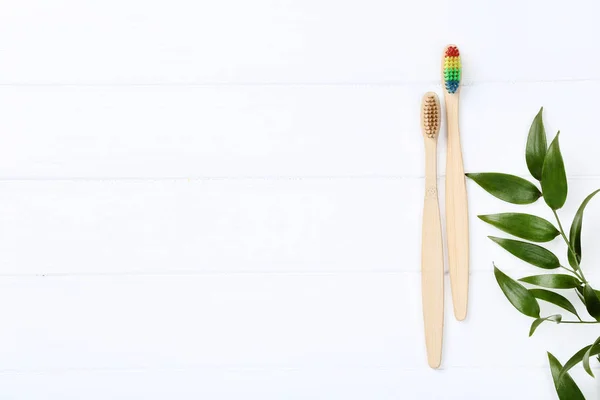 Escovas de dentes de bambu com folhas verdes na mesa de madeira — Fotografia de Stock