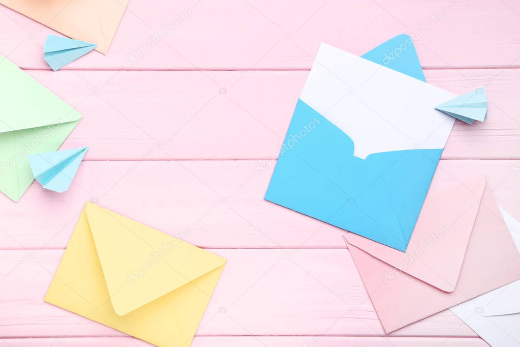 Colorful envelopes with paper planes on pink wooden table