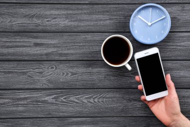 Ahşap üzerinde fincan kahve ve yuvarlak saat ile elle akıllı telefon 