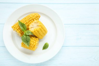 Ahşap masada plaka içinde fesleğen yaprakları ile taze mısır