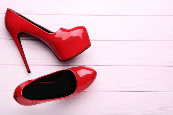 Czerwone buty na wysokim obcasie na różowym drewnianym stole — Zdjęcie stockowe
