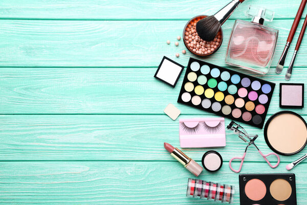 Different makeup cosmetics with perfume bottle on mint wooden ta
