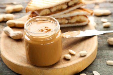 Fıstık ezmesi kavanozda, ekmek ve fındık da tahta masada.