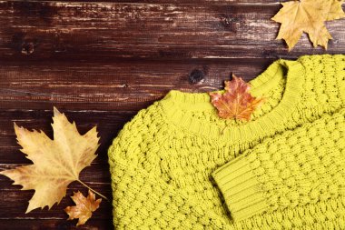 Kahverengi ahşap masa üzerinde sonbahar yaprakları ile örme kazak