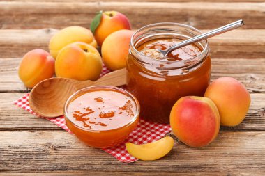 Kahverengi ahşap masa üzerinde kase ve kavanoz kayısı reçeli