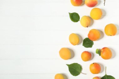 Beyaz ahşap masa üzerinde yeşil yapraklı tatlı kayısı