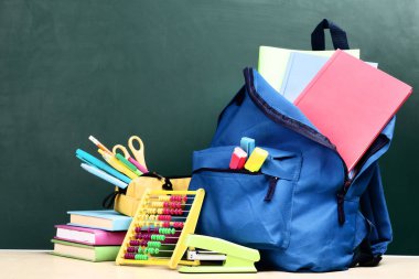 Yeşil arka planda okul malzemeleriyle dolu sırt çantası.