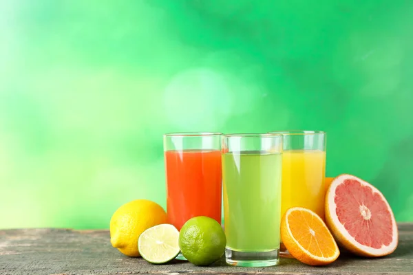 Citrus juice in glasses with fruits on green background — Stock Photo, Image