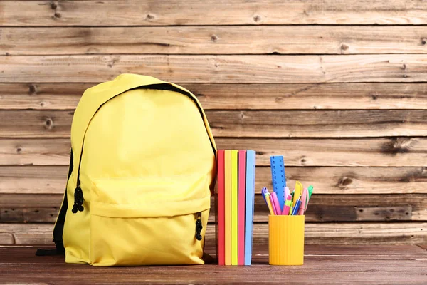 Rucksack mit Notizblöcken und Stiften im Korb auf braunem Holztisch — Stockfoto