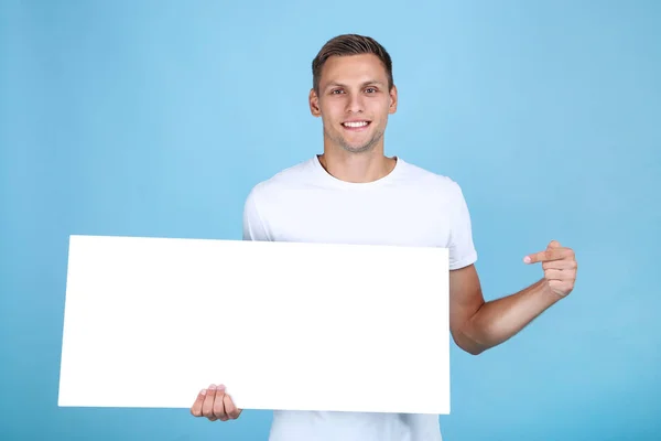 Junger Mann mit leerem Brett auf blauem Hintergrund — Stockfoto