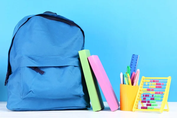 Mochila con útiles escolares sobre fondo azul —  Fotos de Stock