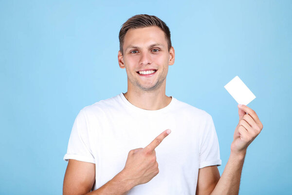 Young man with blank business card on blue background