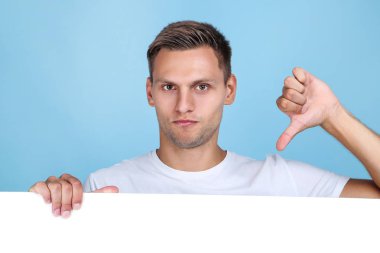 Boş tahtalı ve mavi arka planda başparmağını gösteren genç adam