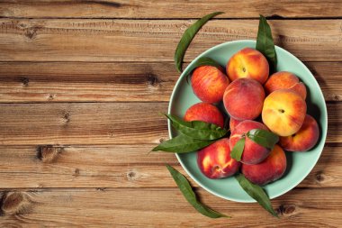 Kahverengi ahşap masa üzerinde plaka yeşil yapraklı taze şeftali