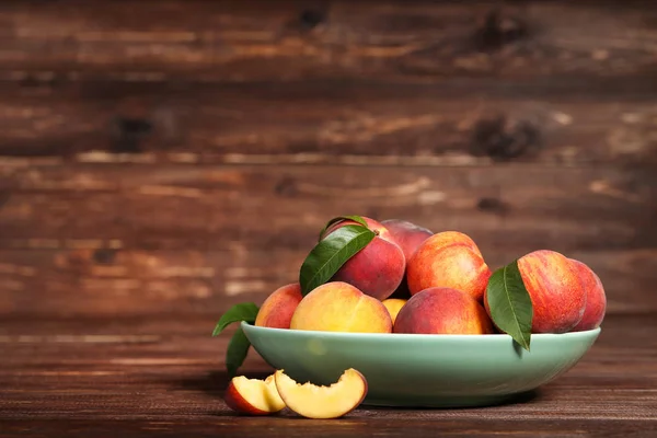 Fresh peaches with green leafs in plate on brown wooden table — Stock Photo, Image
