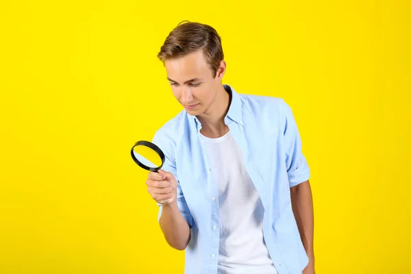 Jonge man met vergrootglas op gele achtergrond — Stockfoto