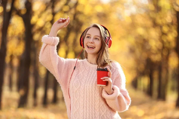 Jong mooi meisje met koptelefoon en papier Cup in de herfst par — Stockfoto