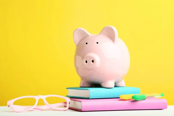Pink piggy bank with glasses and books on yellow background — Stock Photo, Image
