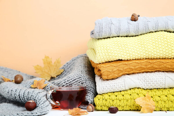 Stack of knitted sweaters with cup of tea and autumn leafs on be